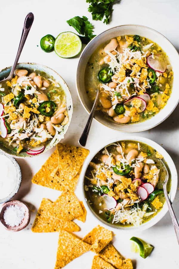 Jalapeno chicken soup in three white bowls with spoons, tortillas on the side.