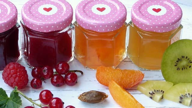 Jams and jellies in a row, surrounded by fresh fruits.