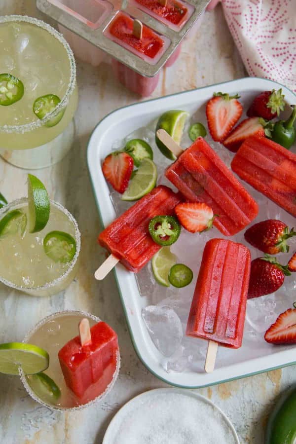 Strawberry jalapeno margarita popsicles over a bowl of ice.
