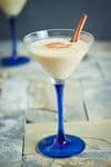 Brandy Alexander in a blue and clear martini glass, with cinnamon stick, on tile.