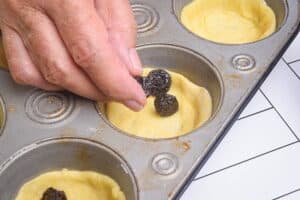 Dough discs in a muffin tray, a hand adding raisins.