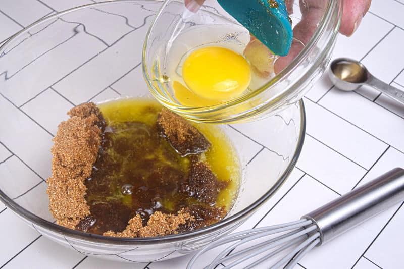Butter, eggs and brown sugar in a bowl, whisk on the side, white background.