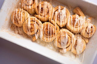 Cinnamon Buns with cream cheese frosting drizzled on top in white serving dish.