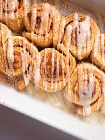 Cinnamon Buns with cream cheese frosting drizzled on top in white serving dish.
