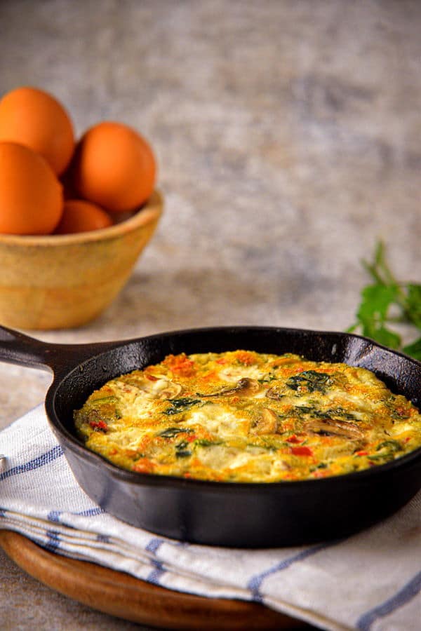 Electric Skillet Vegetable and Goat Cheese Frittata in a cast iron pan, with eggs and cilantro on the side.