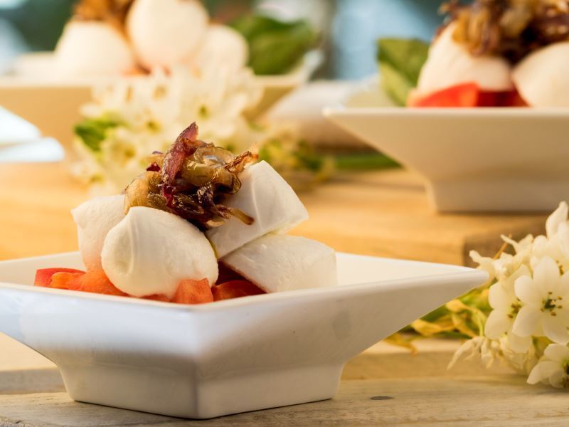 Bocconcini Caprese with Cherry Tomatoes on serving dishes and flowers in the background.
