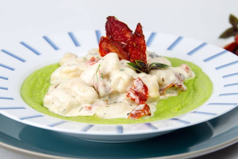 Creamy Gnocchi with Pea Puree 2 Creamy Gnocchi with Pea Puree on a plate, sun-dried tomatoes on the side.