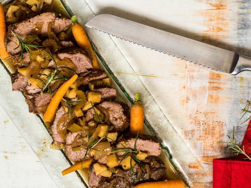 Sliced pot roast on a serving dish with carrots and potatoes.