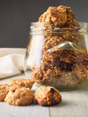 Electric Skillet Oatmeal Cookies in a clear jar, on white wooden background.