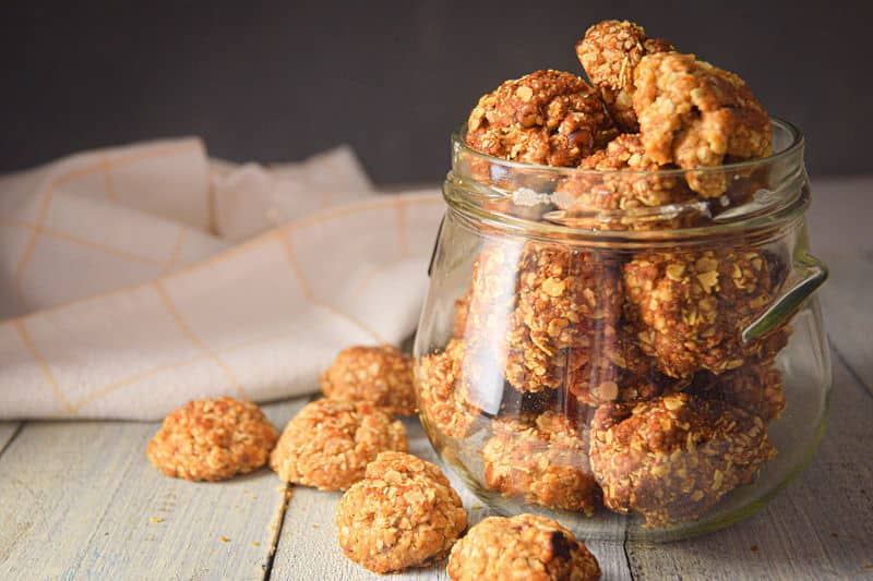 Electric Skillet Oatmeal Cookies in a clear jar, on white wooden background.