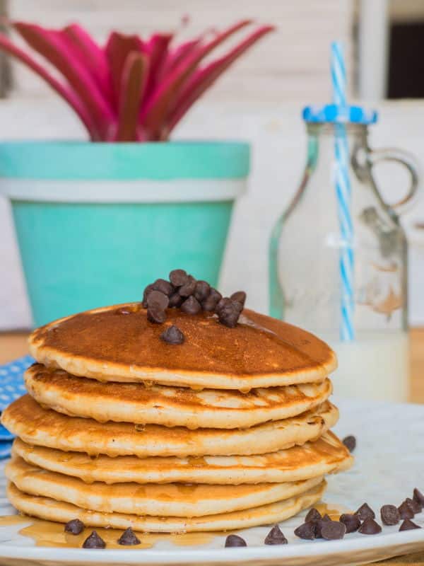 Pancakes piled on a plate with chocolate chips and maple syrup.