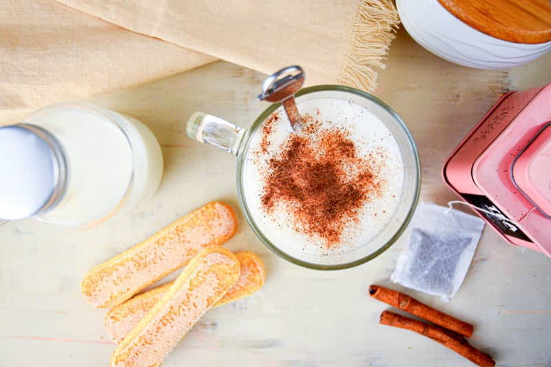 London Fog in a clear glass mug, biscuits, cinnamon and tea bag on the side