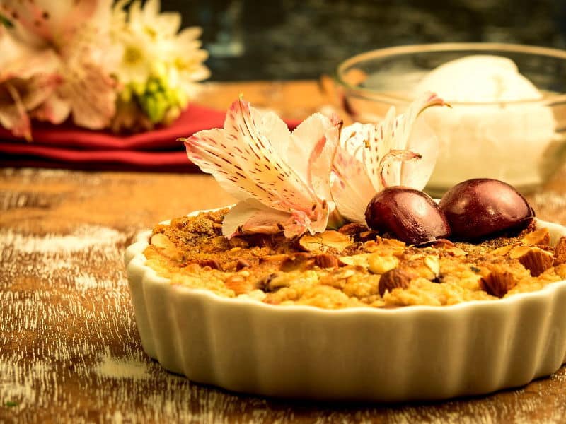 Plum Crumble with Vanilla Ice Cream 1 Plum Crumble with Vanilla Ice Cream in a tart dish with flowers in the background.