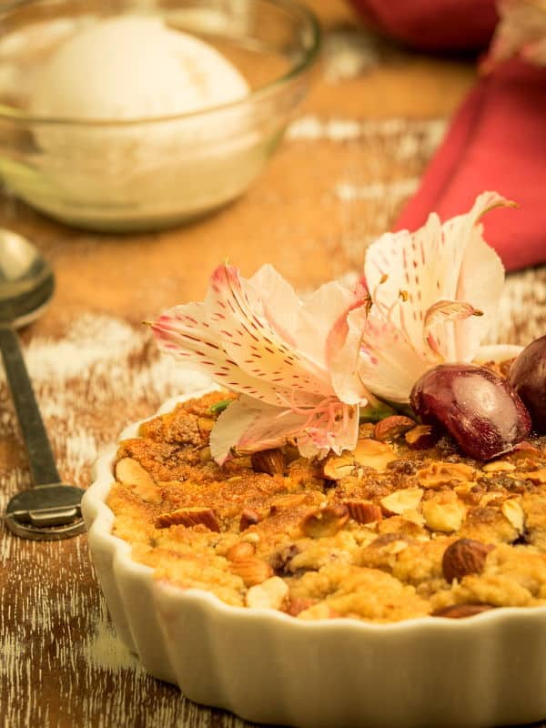Plum Crumble with Vanilla Ice Cream 2 Plum Crumble with Vanilla Ice Cream in a tart dish with flowers in the background.