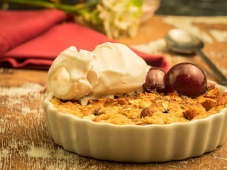 Plum Crumble with Vanilla Ice Cream in a tart dish with flowers in the background.