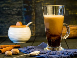 Coffee cream pouring into a mug with cinnamon sticks and sugar jar in the background.