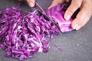 Red cabbage and knife on cutting board, getting shredded.