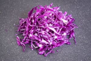 Shredded cabbage on dark speckled cutting board.