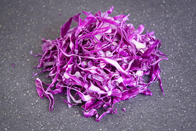 Shredded cabbage on dark speckled cutting board.