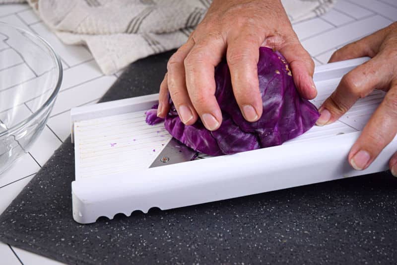 How to Shred Cabbage_25 Shredding red cabbage with mandolin on dark cutting board.