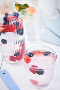 A glass pitcher and glass filled with berries, ice and water.