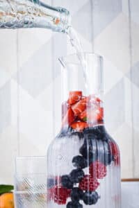 A glass pitcher filled with ice and berries.