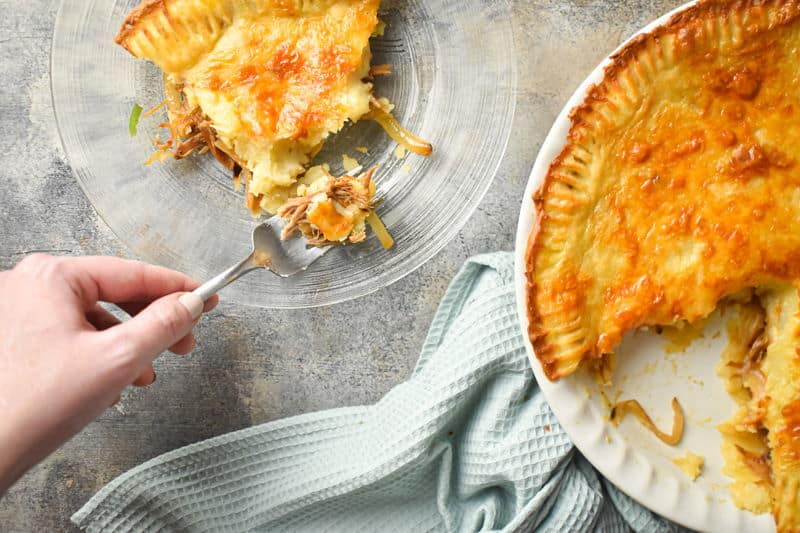 Shepherd's pie on a light towel, and one slice on a clear glass plate with a fork.