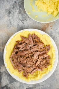 Potatoes, cheese and butter mixture on a plate with shredded lamb.