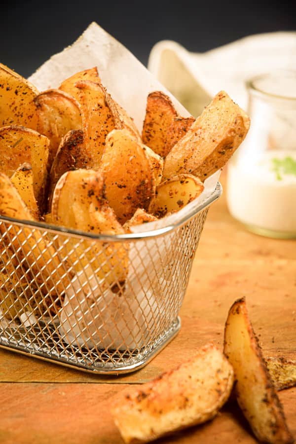 How to Make Cajun Fries 18 Cajun fries in a wire basket, ranch sauce in a jar in the background.