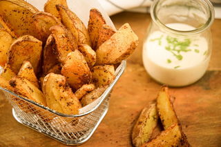 Cajun fries in a wire basket, ranch sauce in a jar in the background.