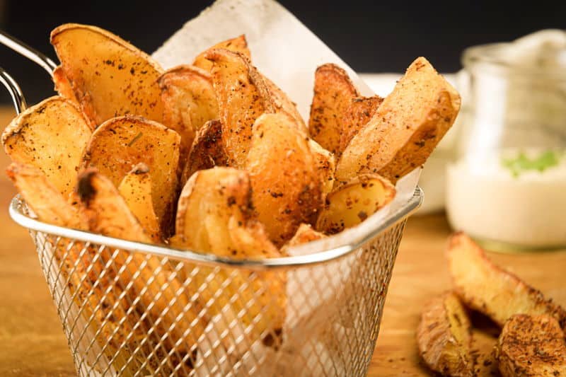 How to Make Cajun Fries 22 Cajun fries in a wire basket, ranch sauce in a jar in the background.