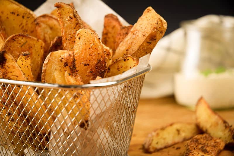 How to Make Cajun Fries 24 Cajun fries in a wire basket, ranch sauce in a jar in the background.
