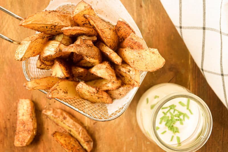How to Make Cajun Fries 27 Cajun fries in a wire basket, ranch sauce in a jar in the background.