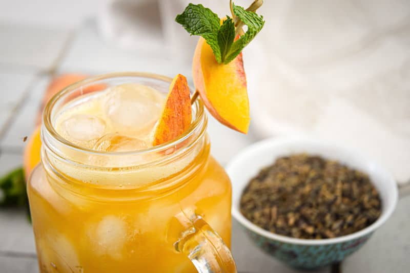 Peachy Iced Green Tea in a mason jar glass, a small bowl of tea leaves on the side.