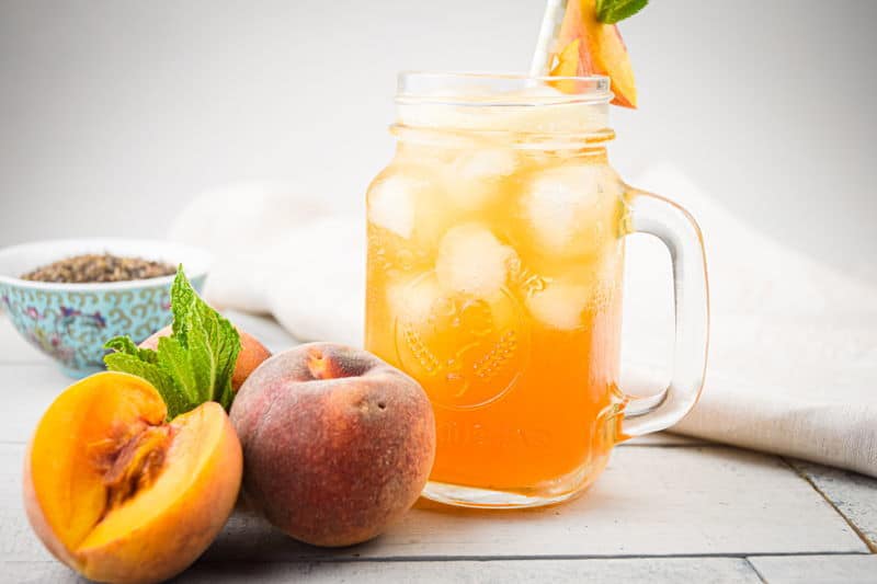 Peachy Iced Green Tea in a mason jar glass, a small bowl of tea leaves and peaches on the side.