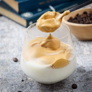 A glass of whipped coffee, coffee beans and books in the background.