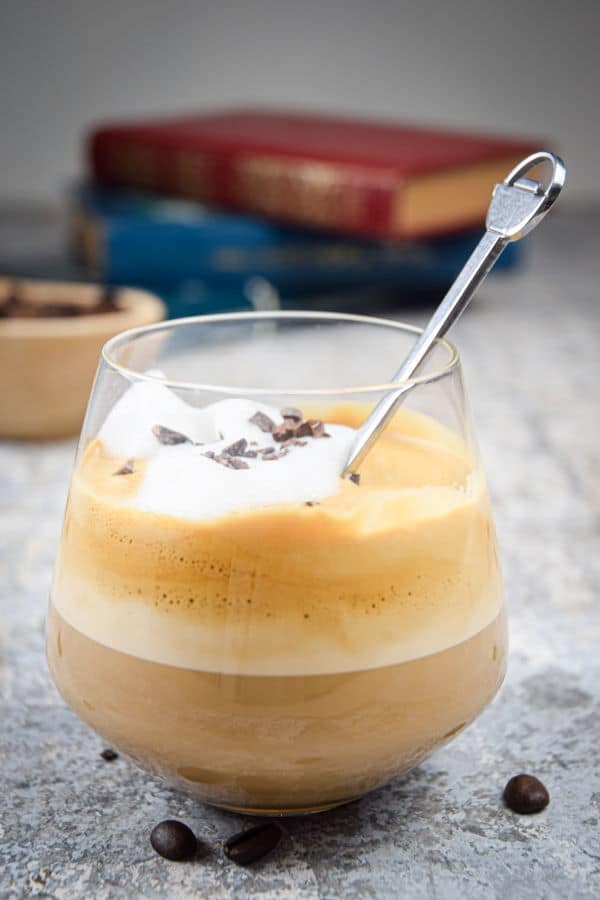 A glass of whipped coffee, coffee beans and books in the background.