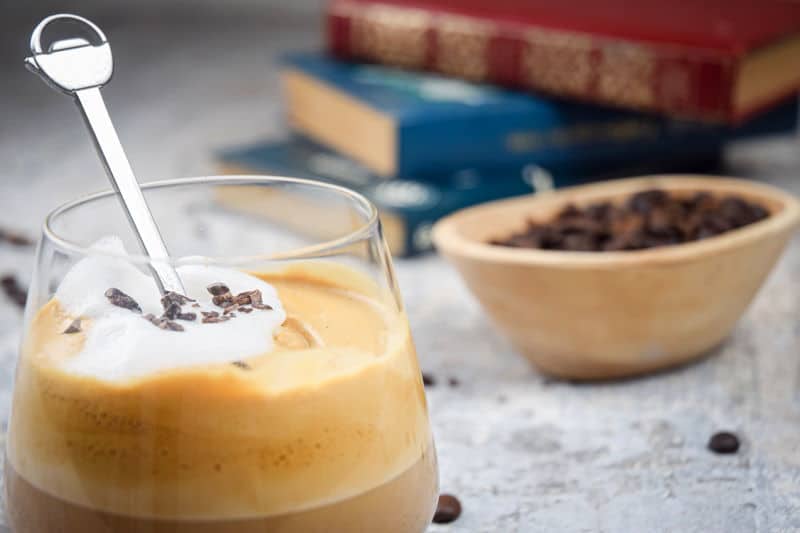 A glass of whipped coffee, coffee beans and books in the background.