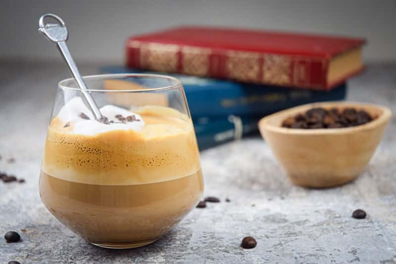 A glass of whipped coffee, coffee beans and books in the background.