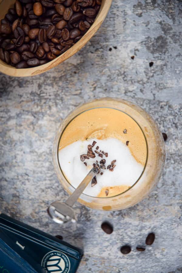 A glass of whipped coffee, coffee beans and books in the background.