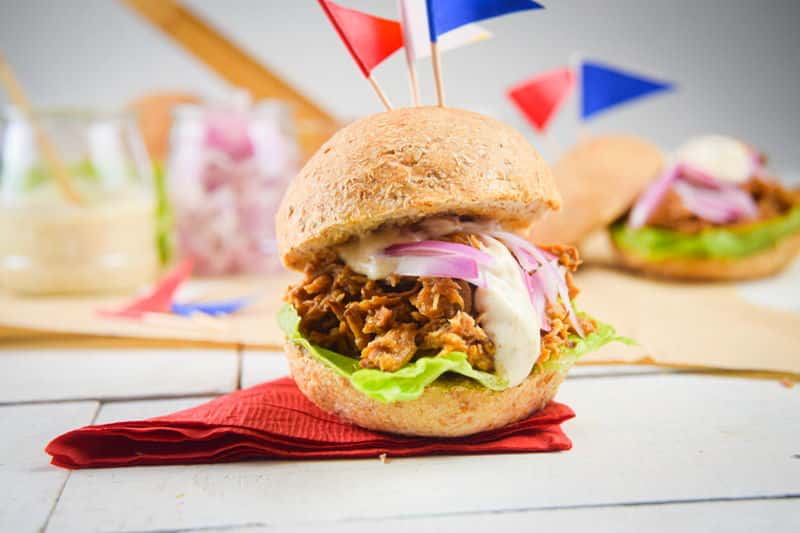 Pulled pork sliders with red white and blue flag toothpicks on white wooden background.