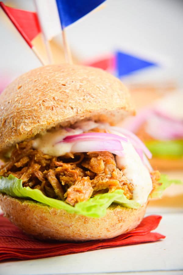 Pulled pork sliders with red white and blue flag toothpicks on white wooden background.