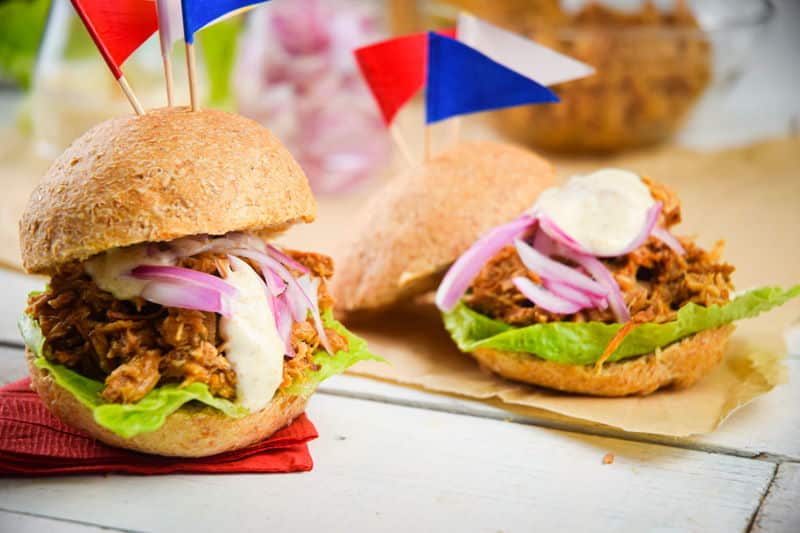 Pulled pork sliders with red white and blue flag toothpicks on white wooden background.