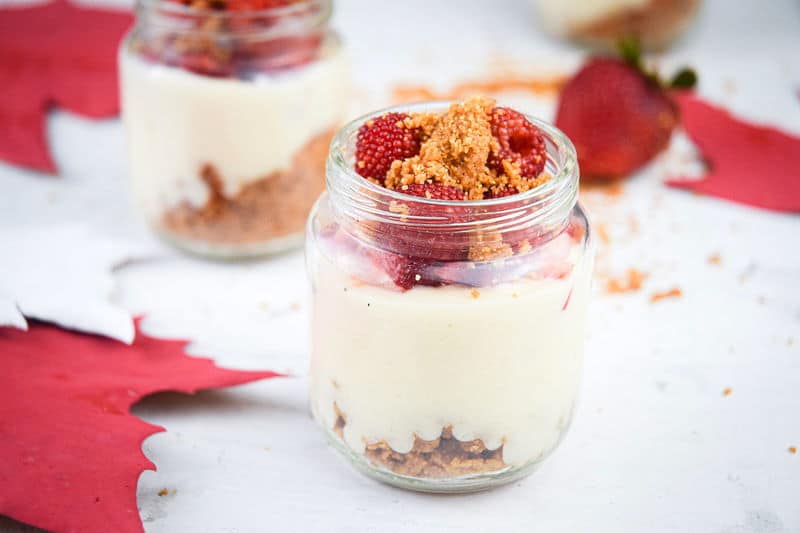 Raspberry cheesecake in mini dessert jars, maple leafs in the background.