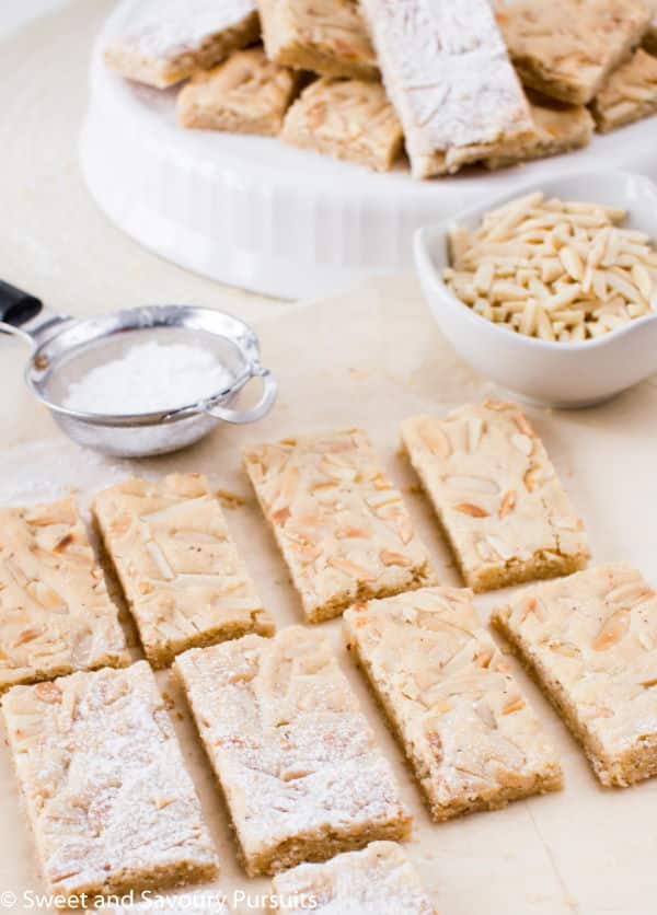 Chewy marzipan bars on parchment, slivered almonds in a bowl.