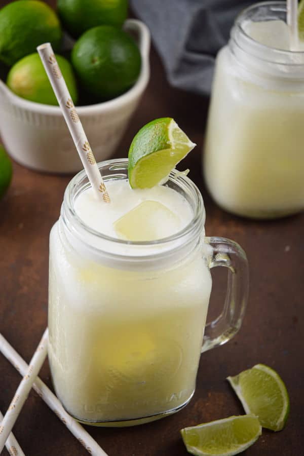 Brazilian Lemonade Suica-9 Brazilian lemonade in glass jars with lime wedges and paper straws, limes in a bowl on the side.