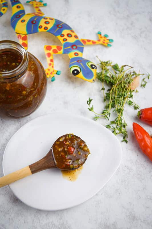 Jerk sauce in a jar with chili peppers, thyme and garlic on the side.