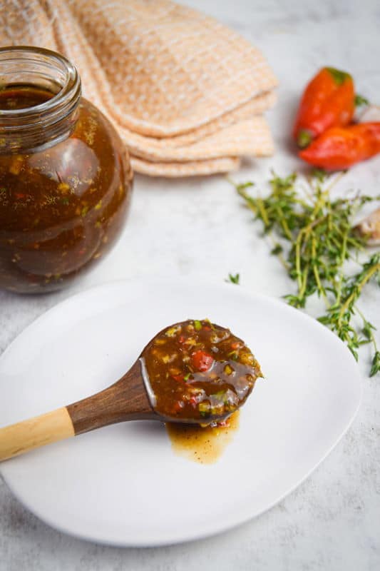 Jerk sauce in a jar with chili peppers, thyme and garlic on the side.