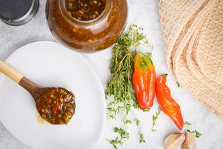 Jerk sauce in a jar with chili peppers, thyme and garlic on the side.