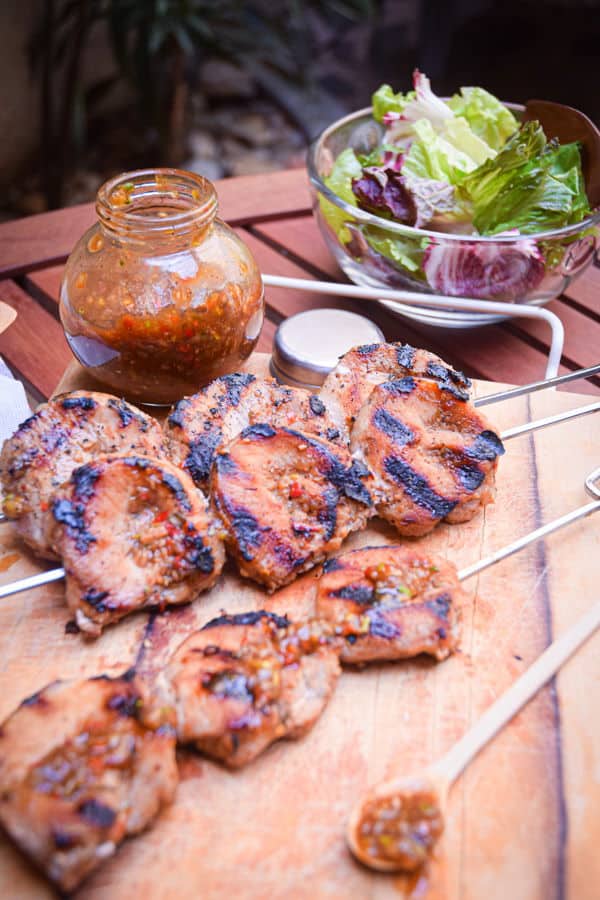 Grilled pork skewers on wooden cutting board with salad and jerk sauce on the side.